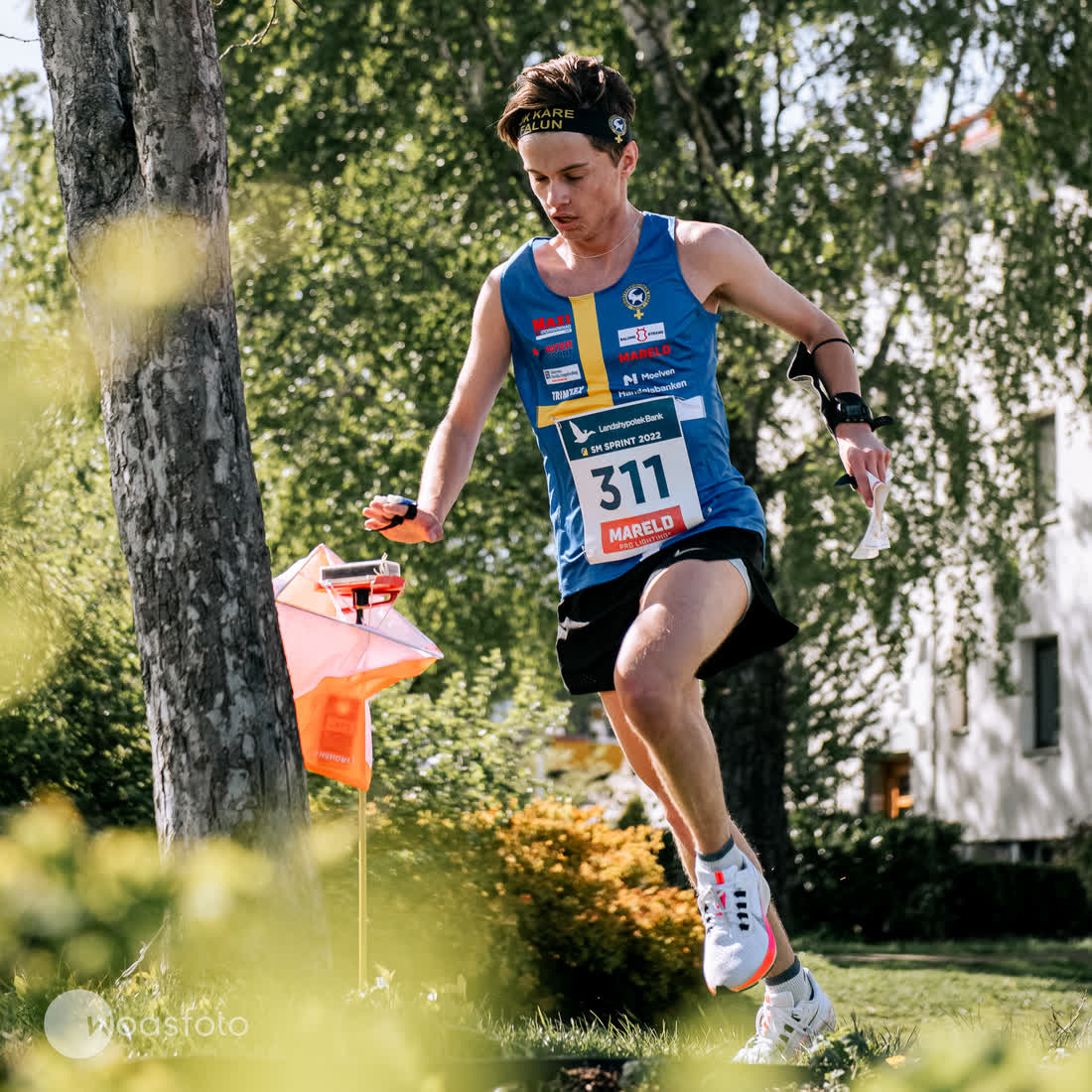 A sprint orienteer punching at an orange control flag
